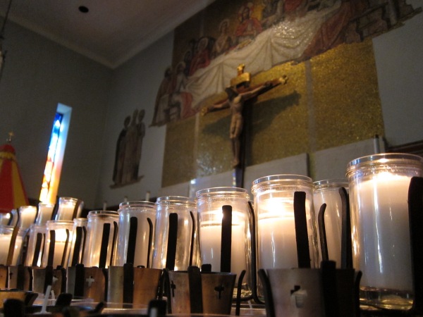 votive candles in the foreground with christ on the cross on the wall in the background; taken at historical basilaca